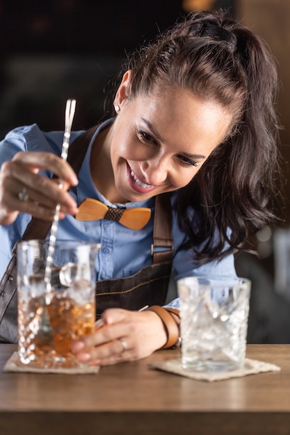 La cameriera sorride mentre mescola cocktail di rum vecchio stile in un bicchiere decorativo in un bar.