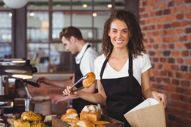 La cameriera sorridente che mette il pane rotola in sacco di carta