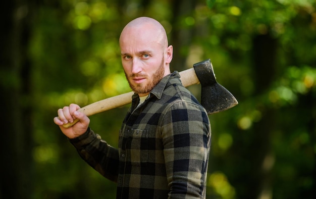 La camicia a scacchi da uomo usa l'ascia. Maschio brutale nella foresta. Potenza e forza. Il boscaiolo porta l'ascia. Boscaiolo calvo. Raccogliere legna da ardere. Escursione vacanza. Escursione nella foresta. Cura della foresta. Determinazione dello spirito umano.