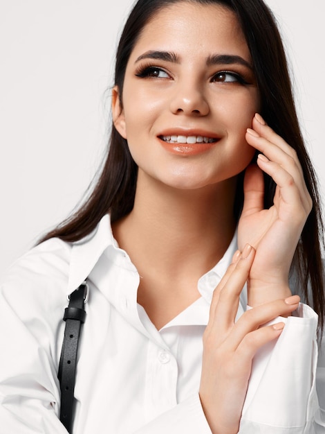 La camicia bianca da donna con bretelle le tocca il viso su uno sfondo chiaro