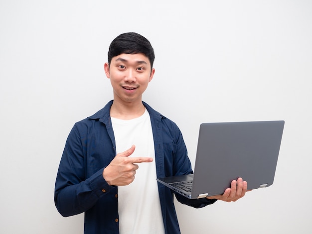 La camicia blu dell'uomo asiatico indica allegramente il dito contro il laptop in mano e guarda la telecamera