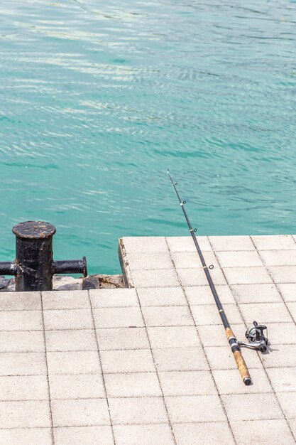 La canna da pesca giace su una piastrella di cemento sullo sfondo del mare