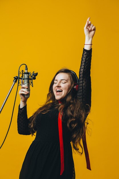 La cantante femminile bruna divertente positiva che si diverte canta una canzone Primo piano di una giovane artista pop caucasica in cuffia sorridente mentre esegue una canzone gioiosa nel microfono sullo sfondo giallo