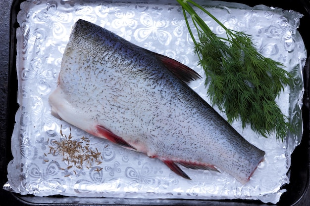 La carcassa di pesce sbucciato giace su un deco. Carpa su lamina d'argento con spezie. Pronto da cuocere alla griglia