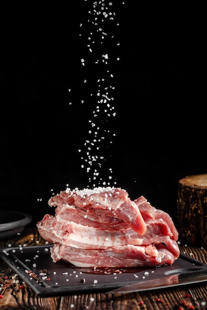 La carne di maiale cruda giace su un tagliere, su un tavolo di legno, accanto a un coltello da cucina. Carne sottaceto in spezie. Immagine di sfondo.