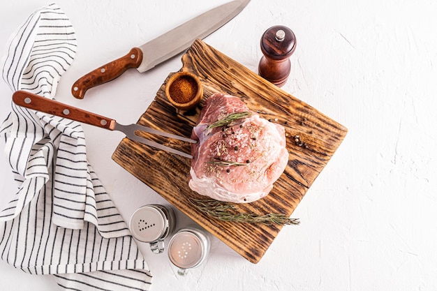 La carne di maiale fresca dell'azienda agricola si trova su una tavola strutturata di legno accanto ai contenitori delle spezie per cucinare la vista superiore del fondo bianco