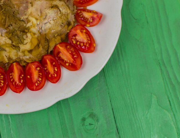 La carne in gelatina in un piatto rotondo decorato con pomodori su una superficie di legno di colore verde chiaro