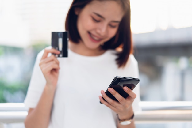 La carta di credito della tenuta della donna paga in linea e facendo uso dello smartphone per il negozio tramite il sito Web. Concetti acquisti online per comodità.