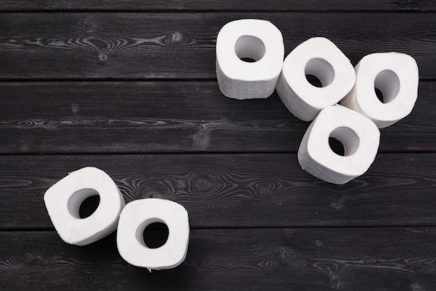 La carta igienica bianca rotola su fondo di legno nero
