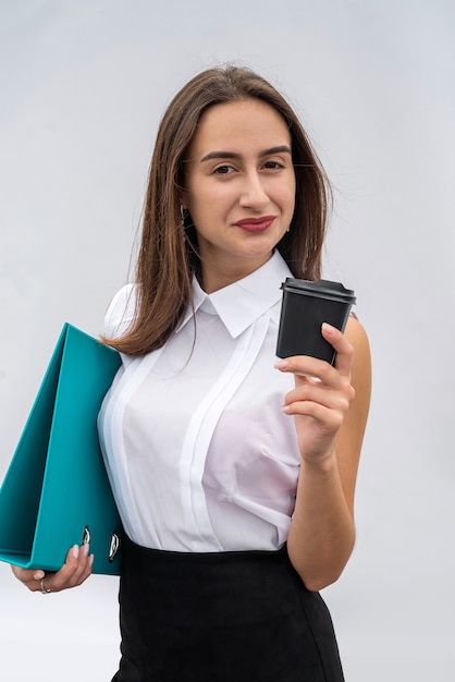 La cartella della tazza della tenuta della giovane donna graziosa indossa la camicia bianca e la gonna nera isolate.