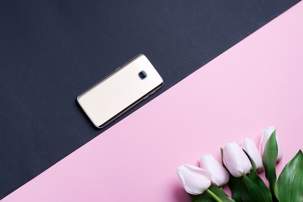 La cartolina d'auguri con il telefono cellulare e i tulipani rosa della molla fioriscono su un fondo diagonale di due tonalità.