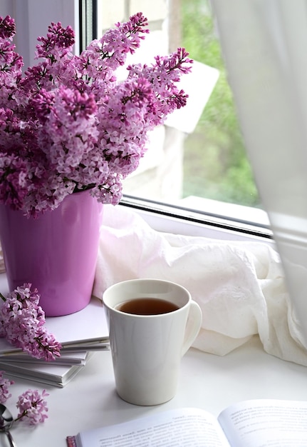 La cartolina è bellissima Una tazza di tè un vecchio libro e un bouquet di lillà viola Una bellissima natura morta Primavera Il concetto di buongiorno