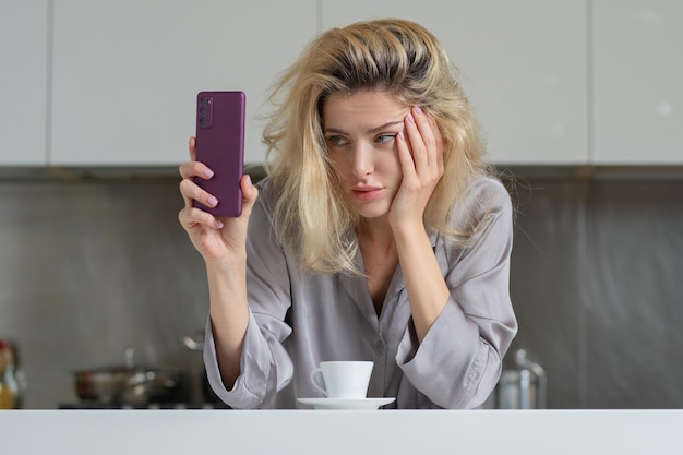 La casalinga infastidita beve caffè in cucina donna triste che chiacchiera al telefono in cucina al mattino