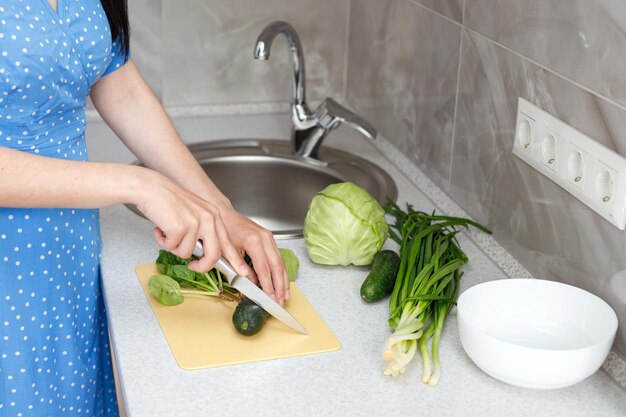 La casalinga taglia un cetriolo con un coltello in un'insalata nel primo piano della cucina