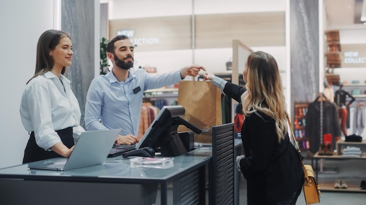Foto la cassiera del negozio di abbigliamento, la bella giovane donna compra una camicia da un amichevole assistente di vendita al dettaglio, riceve una borsa con gli acquisti, un negozio di moda alla moda con marchi di designer.