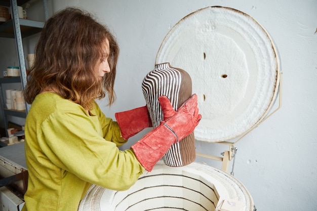 La ceramista tira fuori da un forno dopo la cottura. Maestro ceramista che lavora in studio di ceramica. Processo di creazione della ceramica.