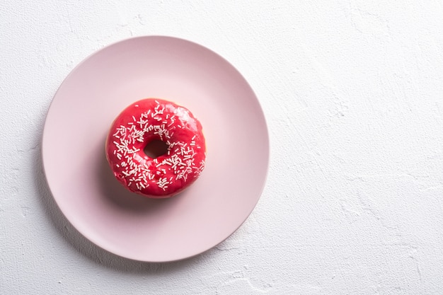 La ciambella rosa con spruzza sul piatto rosa, alimento smaltato dolce del dessert sulla tavola strutturata concreta bianca, spazio della copia di vista superiore