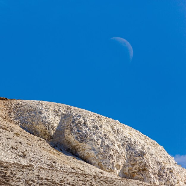 La cima delle montagne di gesso contro un cielo limpido con la luna.