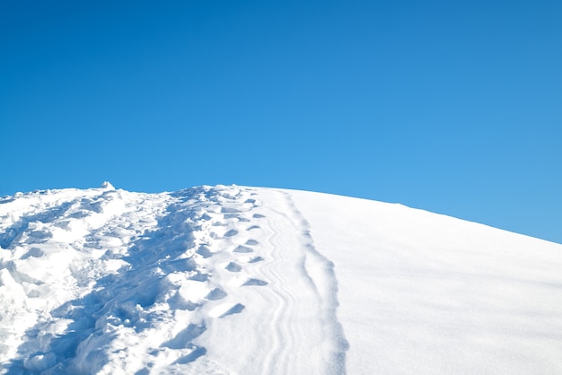 La cima di una collina coperta di neve con un sentiero calpestato e impronte contro il cielo invernale blu