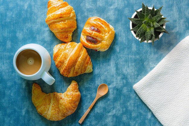 La colazione con i croissant lascia il tagliere e la composizione nel caffè nero con la mano della ragazza su legno