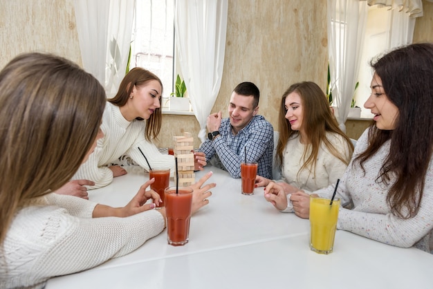 La compagnia di amici beve succo di frutta e gioca al gioco della torre nel caffè