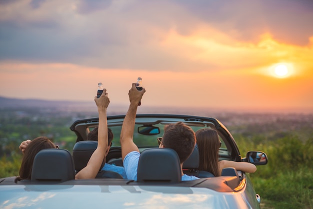 La compagnia di persone si siede in una cabrio sullo sfondo del tramonto