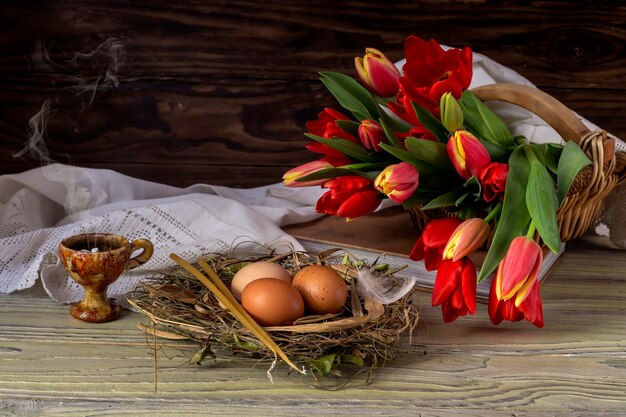 La composizione di pasqua Uova un incensiere di tulipani rossi e candele della chiesa sul primo piano della tavola di legno