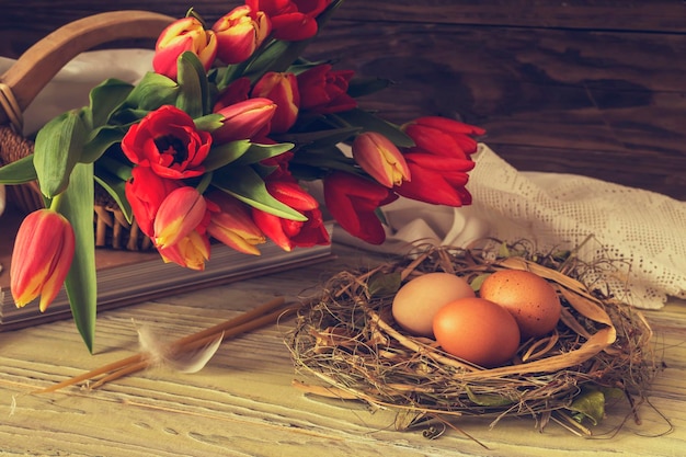 La composizione di pasqua Uova un tulipani rossi e candele della chiesa sul primo piano della tavola di legno