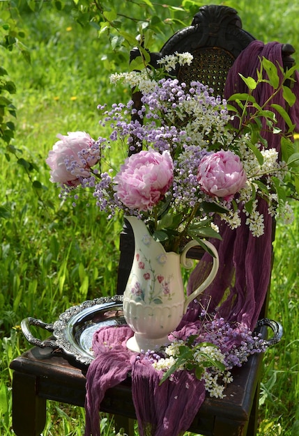 La composizione è un bouquet di peonie in un vaso su una vecchia sedia in giardino.