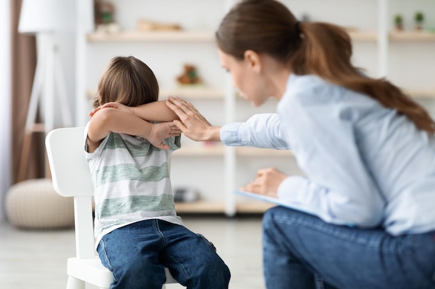 La comunicazione dei bambini blocca il ragazzino spaventato che nasconde il viso dietro le mani ignorando la donna premurosa