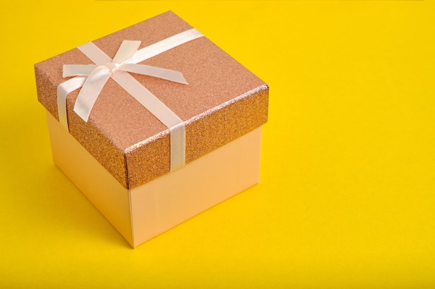 La confezione regalo beige è legata con un nastro con fiocco su sfondo giallo