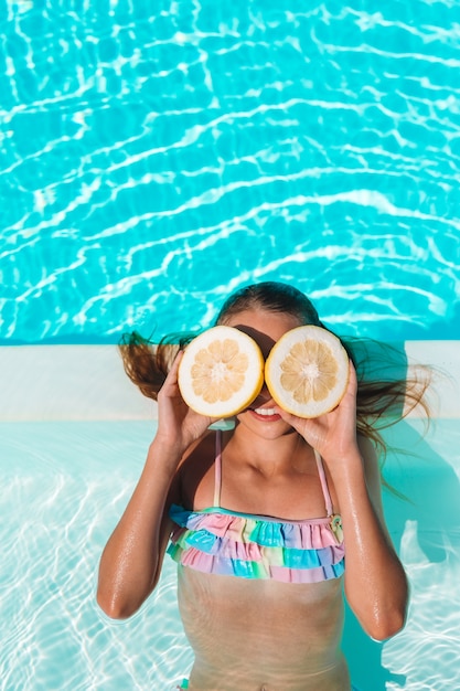 La copertura della bambina osserva con le metà del limone vicino agli occhi sulla piscina del fondo