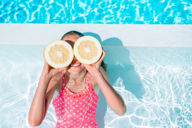 La copertura della bambina osserva con le metà del limone vicino agli occhi sulla piscina