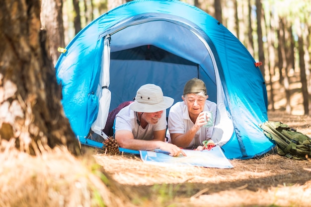 La coppia adulta di viaggiatori caucasici si sdraia all'interno di una tenda mentre sceglie e pianifica su una mappa il prossimo passo del loro viaggio - attività di svago nella natura per i pensionati alternativi