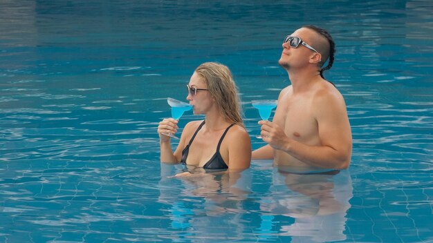 La coppia amorevole abbracci e baci bevendo liquori alcolici cocktail blu nella piscina dell'hotel all'aperto Ritratto di uomo e donna caucasici