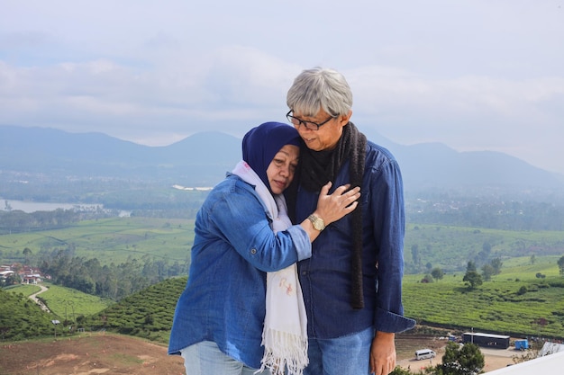 La coppia di anziani romantici asiatici è una vecchia in piedi che abbraccia il marito su un paesaggio drammatico