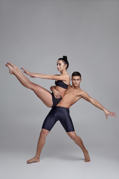 La coppia di una giovane ballerina moderna in abiti neri è in posa su uno sfondo grigio dello studio