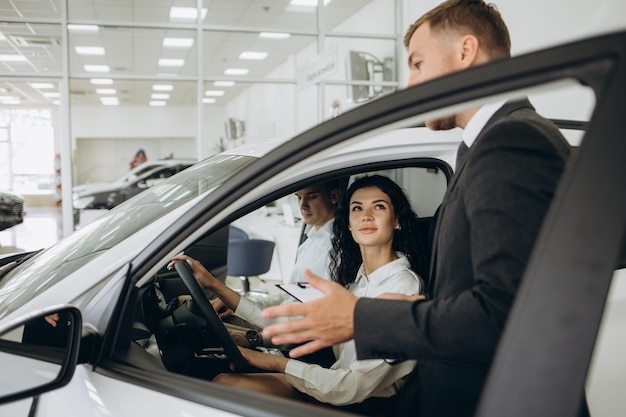 La coppia e il concessionario che vende le auto guardano l'auto nello showroom.