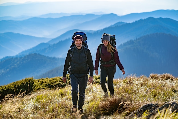 La coppia felice con gli zaini a piedi in montagna