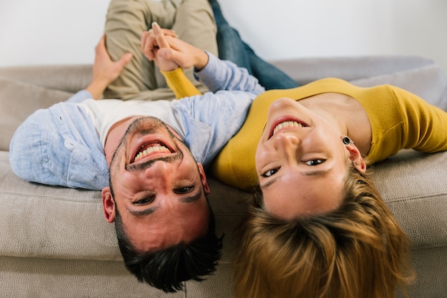 La coppia felice è sdraiata a testa in giù sul divano di casa.