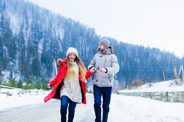 La coppia innamorata si tiene per mano e si diverte mentre corre lungo la strada invernale di montagna