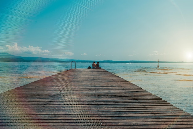 La coppia seduta sul molo con le gambe penzolanti osservava il tramonto sul lago