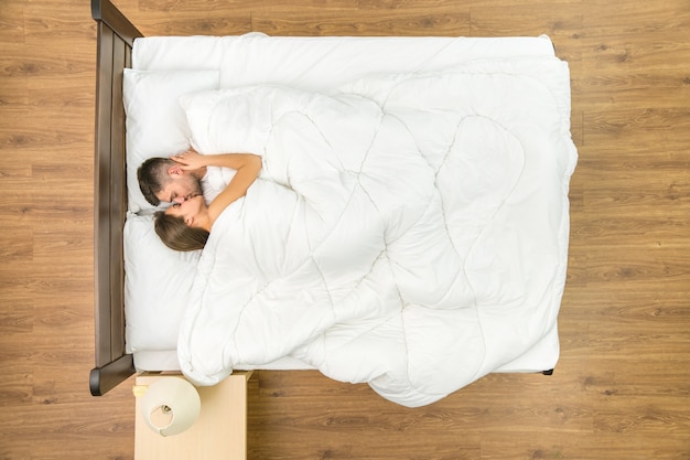 La coppia si bacia sul letto con lenzuola bianche. Vista dall'alto