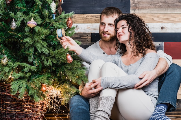 La coppia sorridente romantica si siede vicino all&#39;albero di Natale. Concetto di Natale e Capodanno