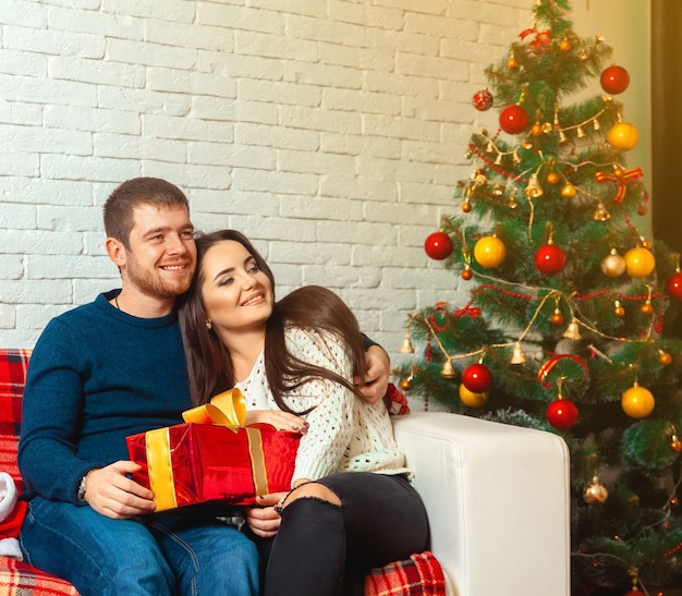 La coppia spensierata con i regali di Natale si siede sul divano. Capodanno. Atmosfera natalizia.