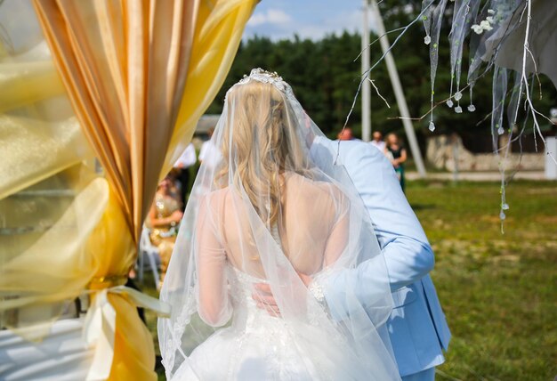 La coppia sta camminando alla cerimonia di nozze all'aperto Sposa e sposo che baciano Arco con fiori