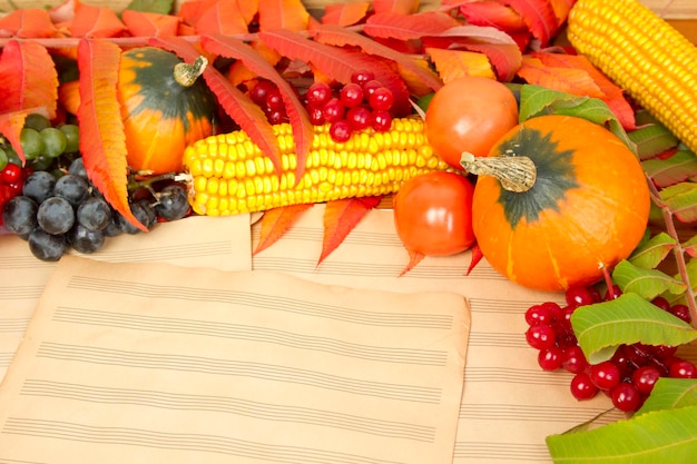 La cornice dei doni dell'autunno zucche mais foglie d'autunno pomodori bacca rossa mirtillo rosso e uva sono nei vecchi fogli di musica stampati