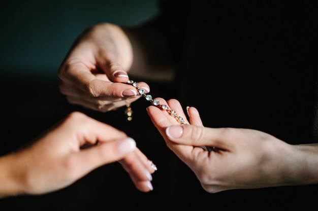 La damigella d'onore aiuta a mettere un braccialetto sul braccio per la sposa. sposa che indossa gioielli, concentrarsi sul braccialetto. Preparazione nuziale per la cerimonia nuziale.