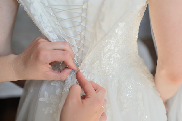 La damigella d'onore aiuta a vestire un abito da sposa in una mattina di nozze