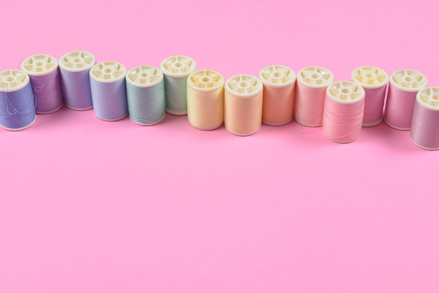 La disposizione piatta del filo colorato rotola per cucire su sfondo rosa